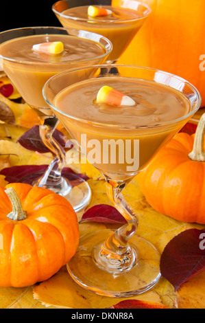 Martini glasses filled with butterscotch pudding decorated with candy corn accompanied by colorful fall leaves and pumpkins Stock Photo