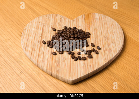 Brown roasted coffee beans on a wooden heart shaped chopping board Stock Photo