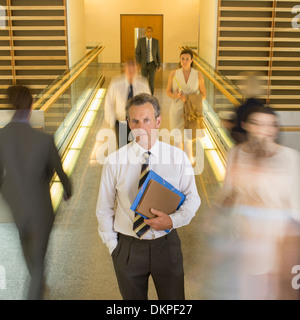 Businessman standing in busy office corridor Stock Photo