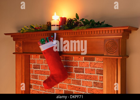 A Christmas stocking full of gifts hanging from a mantelpiece lit by the glow from the fireplace on Christmas Day. Stock Photo