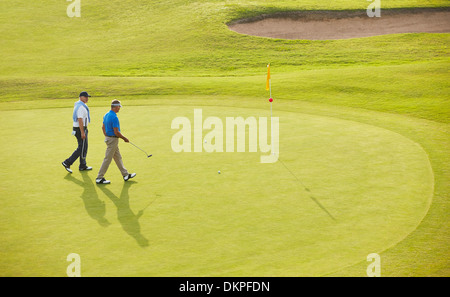 Senior men walking toward flag and hole on golf course Stock Photo