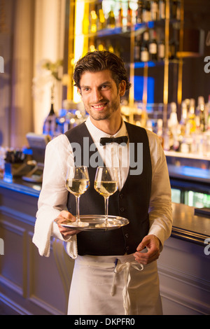 Well dressed bartender carrying wine glasses on tray in luxury bar Stock Photo