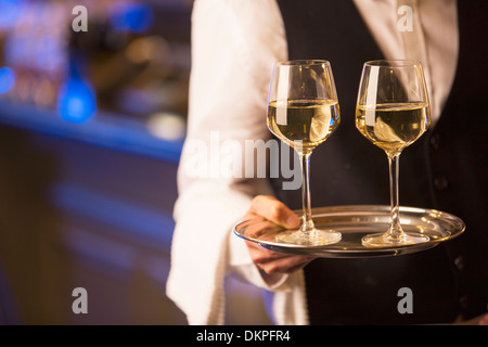 Close up bartender carrying white wine glasses on tray Stock Photo