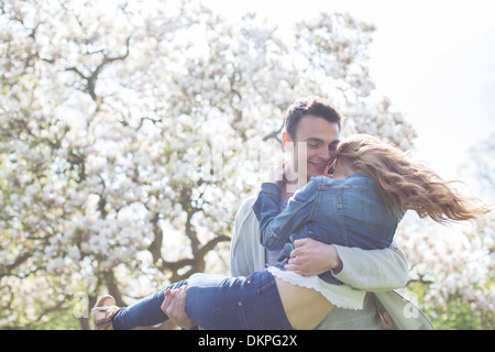 Man lifting woman under tree with white blossoms Stock Photo
