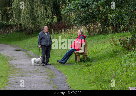 Two senior men talking and passing the time of day, one man is taking his dog for a walk. Stock Photo