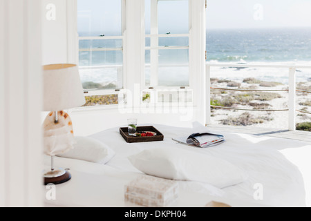 Breakfast tray and magazine on bed overlooking ocean Stock Photo