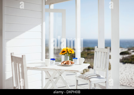 Vase of flowers, coffee and pastries on patio table overlooking ocean Stock Photo