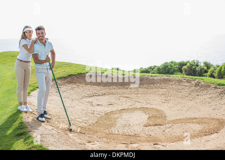Couple drawing heart-shape in sand trap on golf course Stock Photo