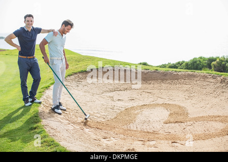 Men raking heart-shape in sand trap on golf course Stock Photo