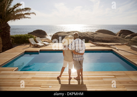 Senior couple hugging by modern pool overlooking ocean Stock Photo