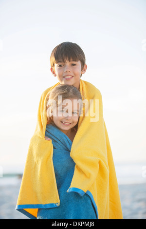 Brother and sister wrapped in towels on beach