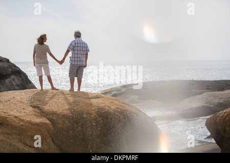 Senior couple holding hands on rocks at beach Stock Photo