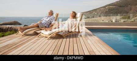 Older couple relaxing in lawn chairs by pool Stock Photo