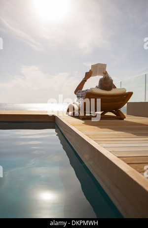 Man reading in lawn chair by pool Stock Photo