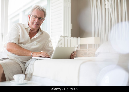 Older man using laptop on bed Stock Photo
