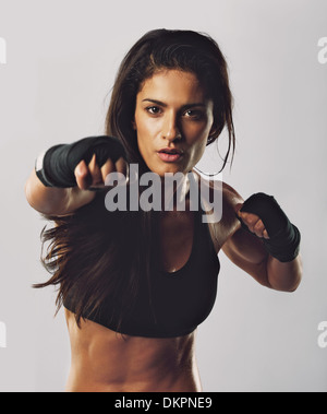 Portrait of young sport girl training boxing against grey background. Hispanic female practicing boxing looking at camera. Stock Photo