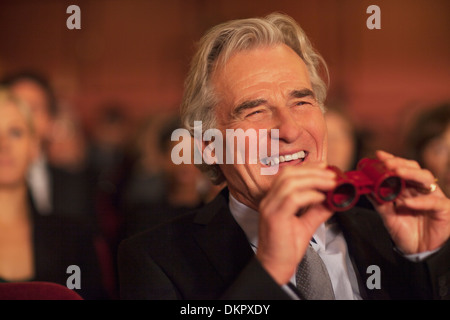 Man with opera glasses laughing in theater audience Stock Photo