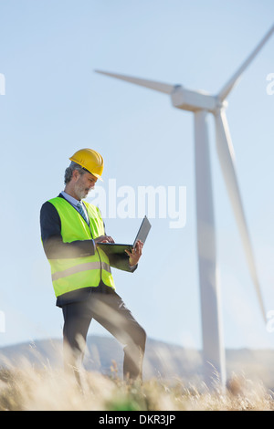 Worker using laptop by wind turbine in rural landscape Stock Photo