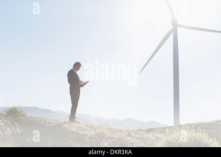 Businessman using laptop by wind turbine in rural landscape Stock Photo
