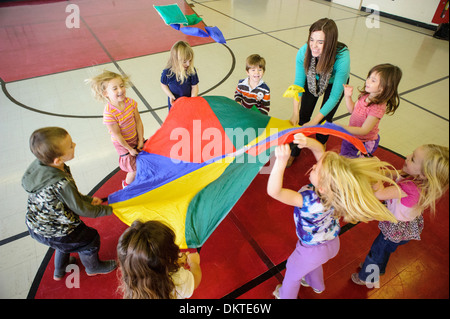 Pre-school children playing with rainbow parachute in gym Stock Photo