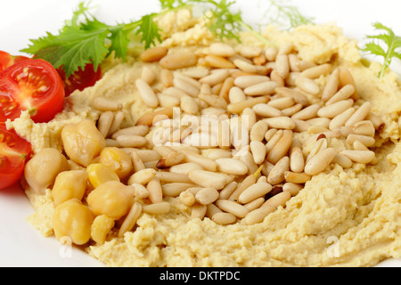 Hummus and lightly roasted pine-nuts dip, garnished with cherry tomatoes and young salad leaves, viewed close-up Stock Photo
