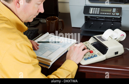 Horizontal photo with focus on male hand while using calculator with tax tables and other office equipment in background Stock Photo