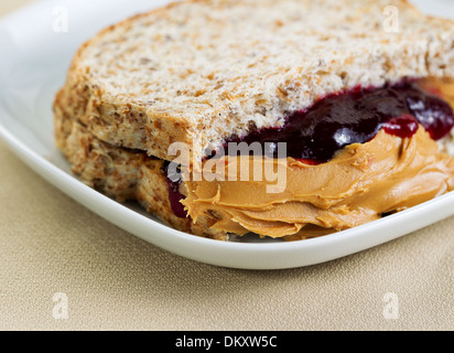 Closeup horizontal photo of a peanut butter and jelly sandwich cut in half, inside white plate on textured table cloth Stock Photo