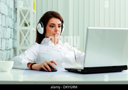 Young businesswoman in headphones working on a laptop at office Stock Photo