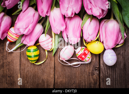Tulips and eggs border over wooden backdrop. Easter decorations. Stock Photo