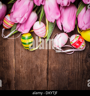 Tulips and eggs border over wooden backdrop. Easter decorations. Stock Photo