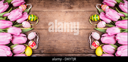 Tulips and eggs border over wooden backdrop. Easter decorations. Stock Photo