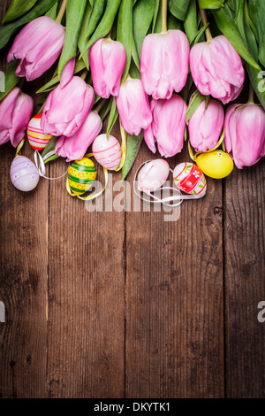 Tulips and eggs border over wooden backdrop. Easter decorations. Stock Photo