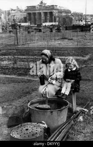 A woman is pictured with her daughter eating breakfast in her 'garden' near the Brandenburg Gate in Tiergarten in Berlin, Germany, in 1946. In the postwar period, the trees and bushes of Tiergarten were used as fuel due to the coal deficiencies. On the open ground, potatoes and vegetables were grown, which was officially allowed as a temporary solution by the British occupation forces: around 2550 parcels were created. Fotoarchiv für Zeitgeschichte Stock Photo