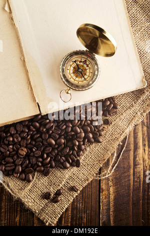 Coffee beans and compass on open book on jute canvas texture. Stock Photo