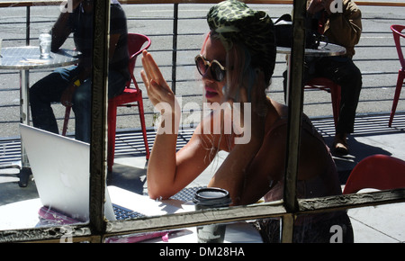 woman in coffee shop talks on iphone and works on laptop in san francisco Stock Photo