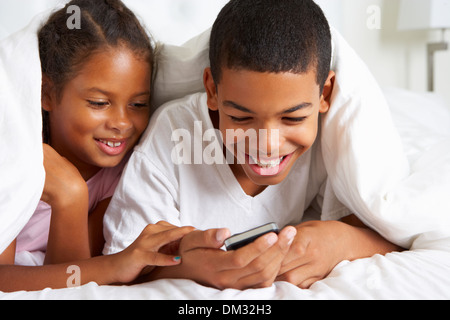 Two Children Using Mobile Phone Under Duvet Stock Photo