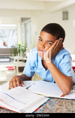 Fed Up Boy Doing Homework In Kitchen Stock Photo