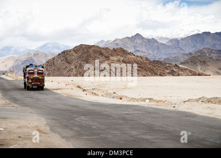 Ladakh, India - 13 July 2009: a colorful lorry travels on a remote road surrounded by high mountains. Dramatic clouds and sky. Stock Photo