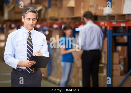 Manager In Warehouse Writing On Clipboard Stock Photo