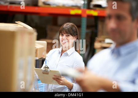 Manager In Warehouse With Worker Scanning Box In Foreground Stock Photo