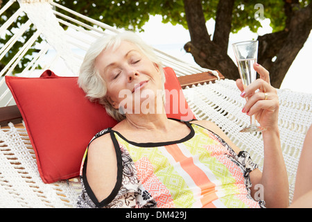 Senior Woman Relaxing In Beach Hammock With Champagne Stock Photo