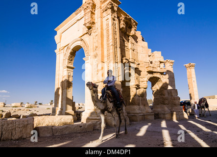 Man on camel beside the monumental arch of the ruins at Palmyra, Syria Stock Photo