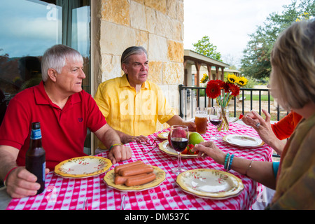 Two retired couples at a backyard barbecue party. Food and drinks, like fresh fruit, sausages, beer and wine, on the table. Stock Photo