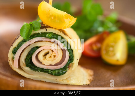 Crepe roll as finger food filled with spinach and ham garnished with cherry tomato and watercress served on wooden plate Stock Photo