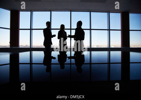 Outlines of three office workers interacting by the window Stock Photo