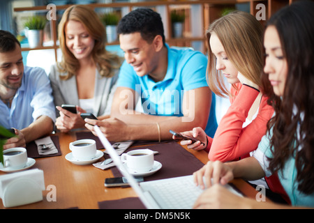 Portrait of teenage friends using modern gadgets while sitting in cafe Stock Photo