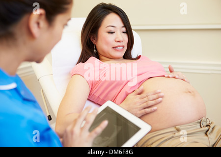 Nurse Using Digital Tablet In Meeting With Pregnant Woman Stock Photo