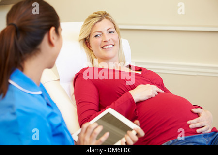 Nurse Using Digital Tablet In Meeting With Pregnant Woman Stock Photo