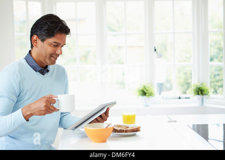 Indian Man Using Digital Tablet Whilst Eating Breakfast Stock Photo