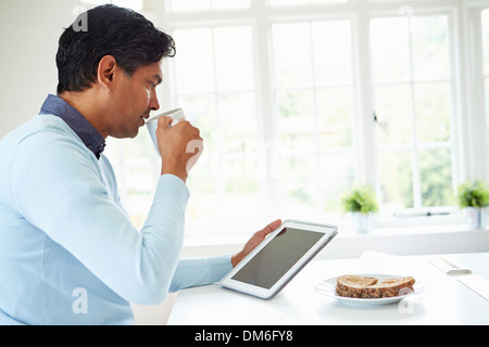 Indian Man Using Digital Tablet Whilst Eating Breakfast Stock Photo